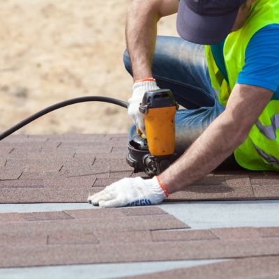 Roofer builder worker with nail gun installing Asphalt Shingles